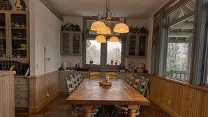 A dining room with a wooden table and blue chairs, a chandelier, and large windows with a view of trees. - Eagles Rest:Mountain views>Huge home>Hiking (#23-ZONE3439) (Estes Park)