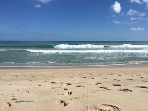 A beach with footprints in the sand and waves crashing onto the shore.
