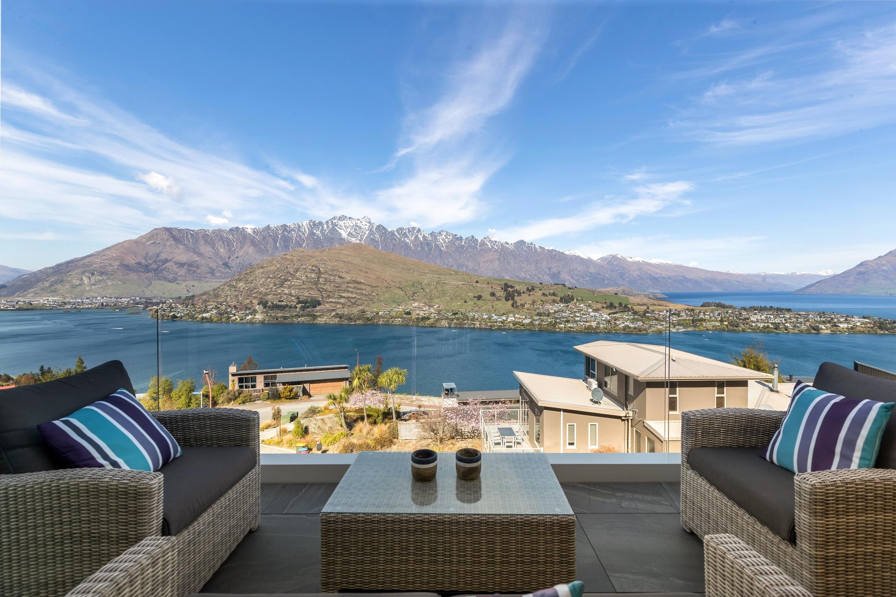 A balcony with wicker furniture and a view of a lake and mountains.