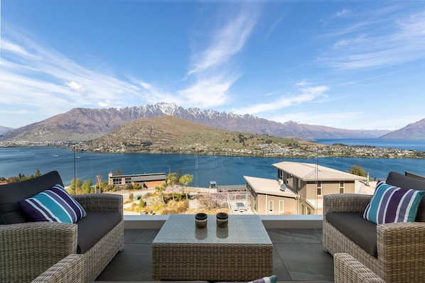 A balcony with wicker furniture and a view of a lake and mountains.