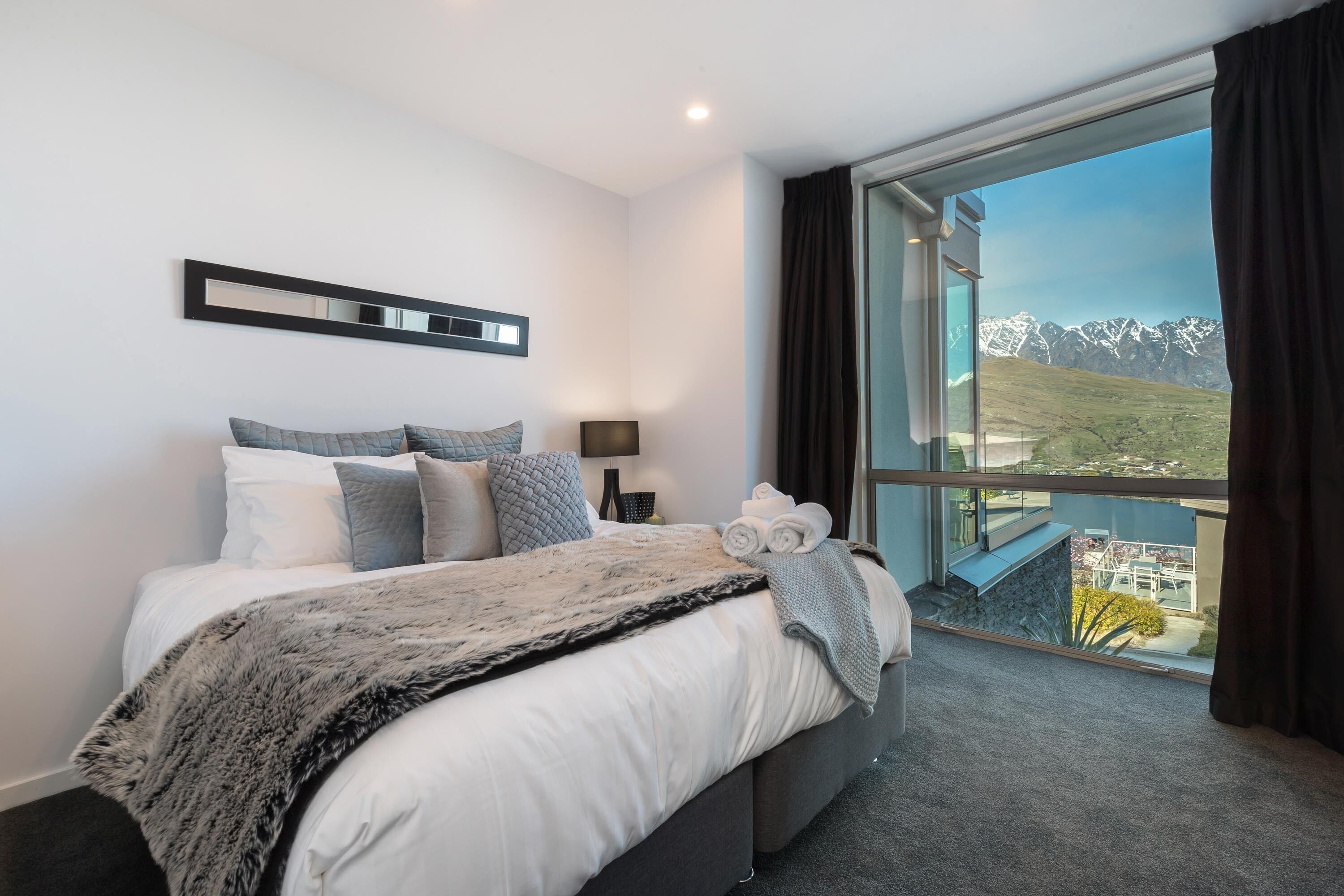 A modern hotel room with a large bed, a view of mountains, and a balcony with a glass door.