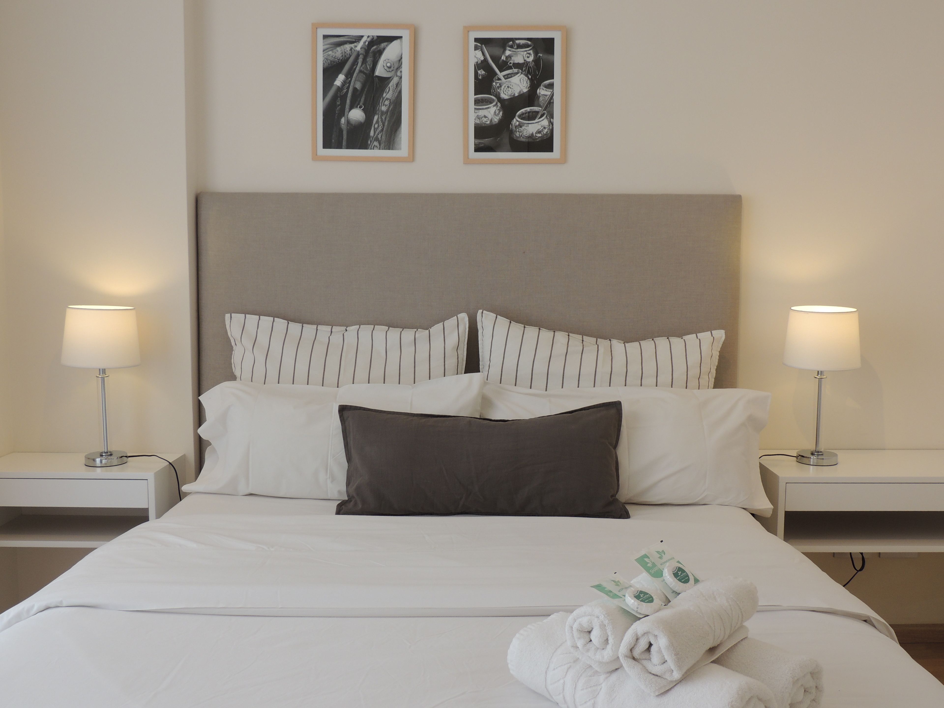 Una cama bien hecha con almohadillas blancas y a rayas, dos lámparas de noche y un cabecero.