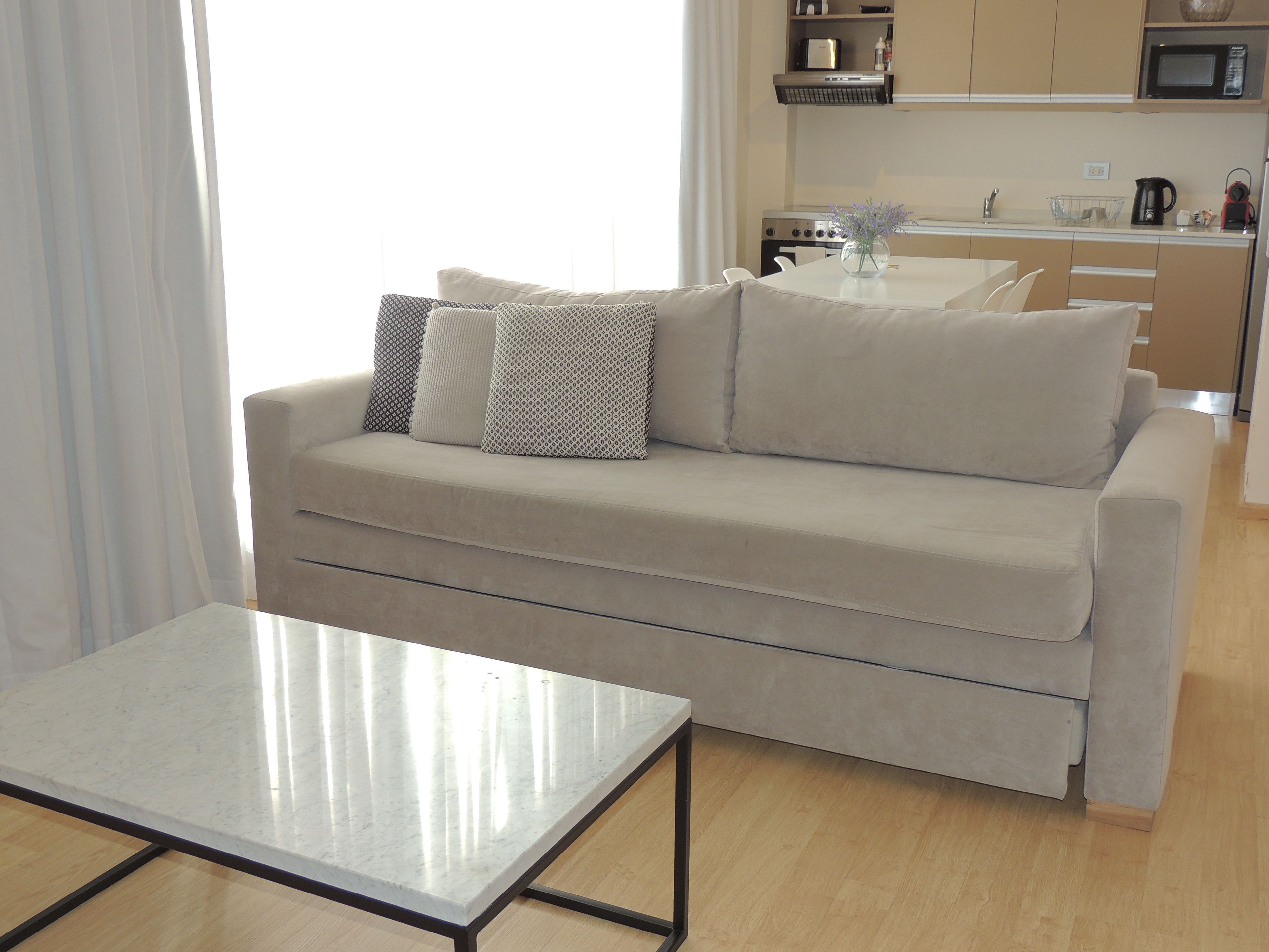 A modern living room with a sofa, a coffee table, and a kitchen in the background.