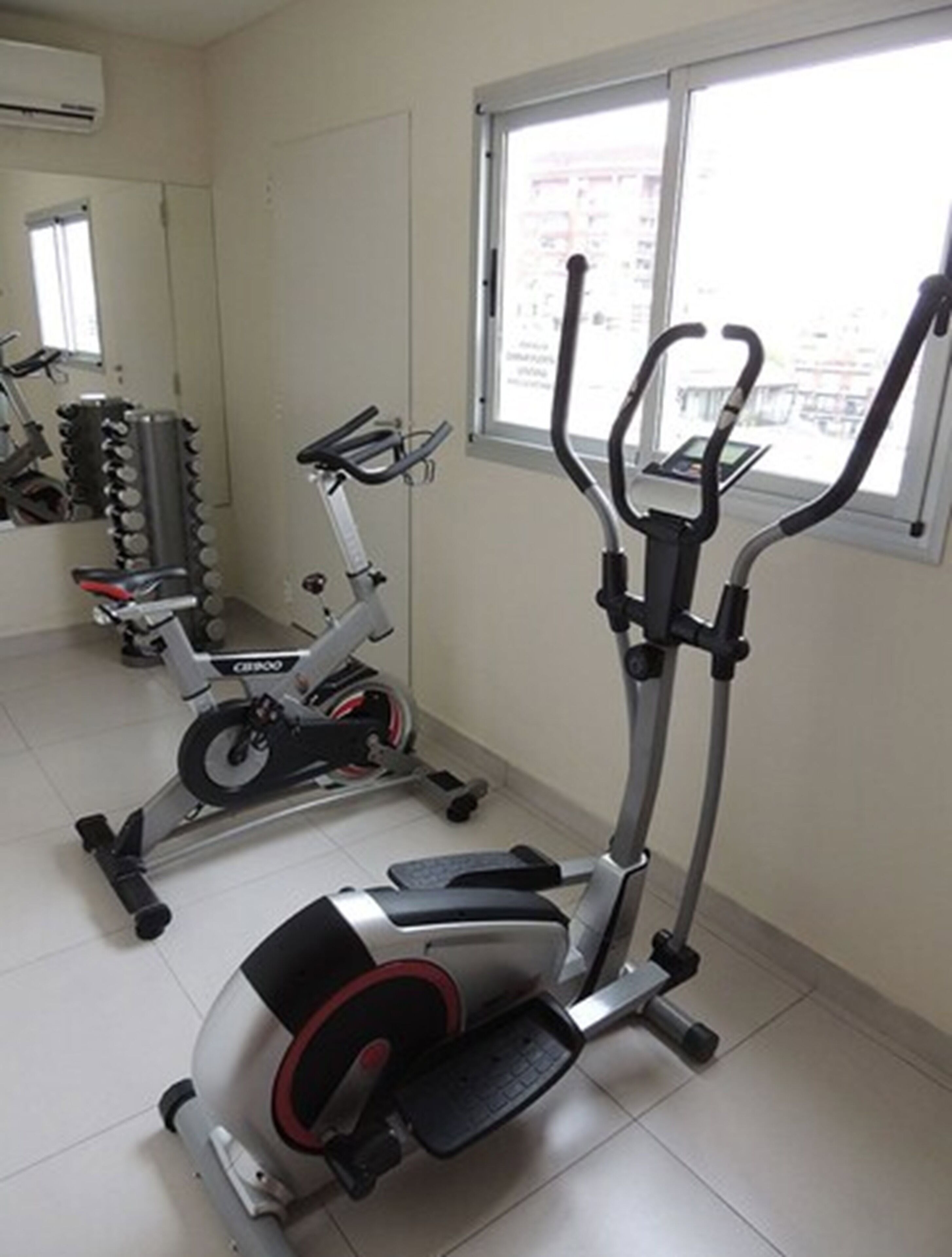 A gym with cardio machines, a mirror, and a window with a view of buildings.
