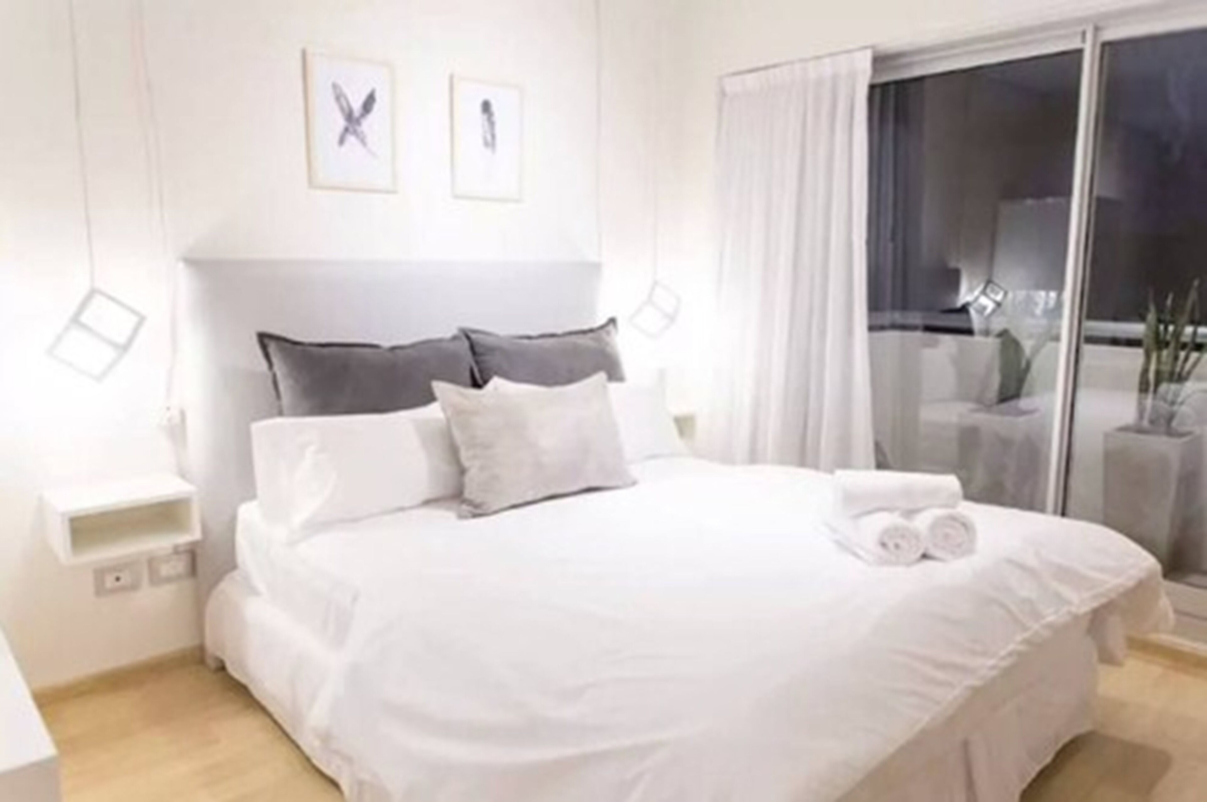 Een net opgemaakt bed met witte beddengoed en kussens, een nachtkastje en uitzicht op de omgeving door een glazen deur.