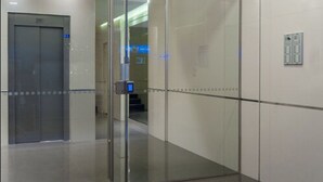 Un ascensor moderno con pantalla digital, puerta de vidrio y panel de control en la pared.