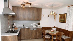 A compact kitchen with wooden cabinets, a built-in dishwasher, a coffee maker, and a dining area with a bench and chairs. - Apartment 2 - Bocksleitnerhof (Wackersberg)