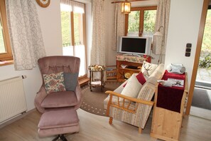 Una sala de estar acogedora con un sillón mullido, un sofá de madera, una mesita con un televisor y un radiador.