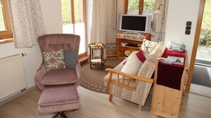 A cozy living room with a cushioned chair, a wooden sofa, a small table with a television, and a radiator. - Apartment 2 - Bocksleitnerhof (Wackersberg)