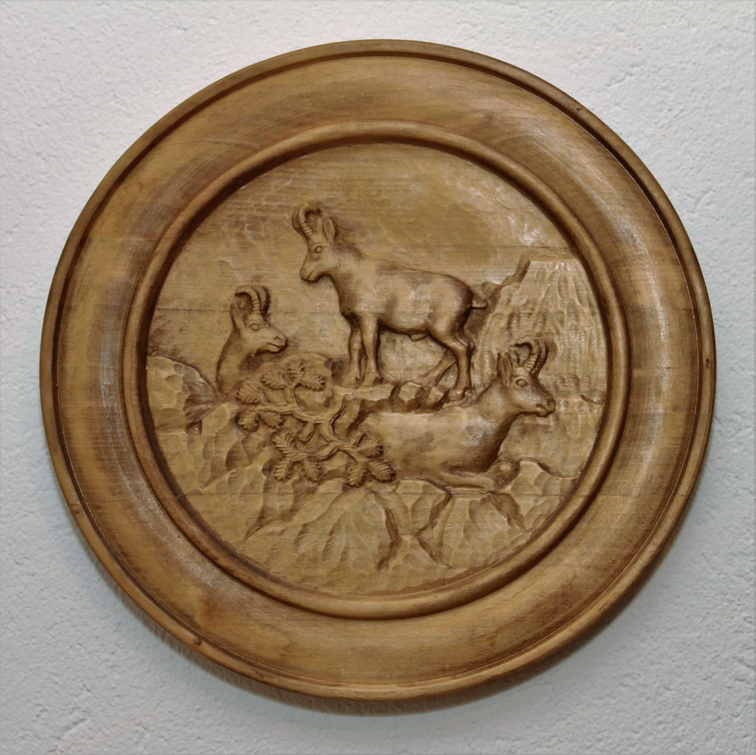 Une assiette en bois ornée d’une scène sculptée représentant des animaux et des feuillages.