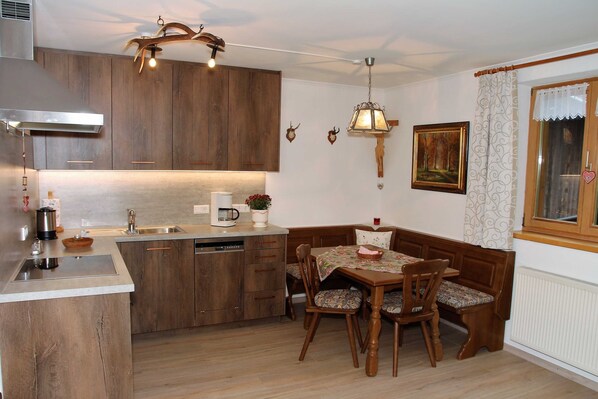A kitchen with wooden cabinets, a built-in dishwasher, a dining table with chairs, and a pendant light. - Apartment 2 - Bocksleitnerhof (Wackersberg)