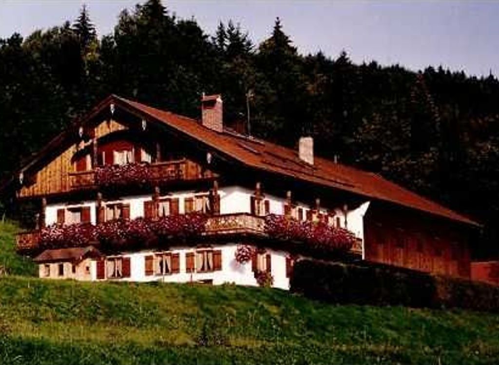 Ein zweistöckiges Holzhaus mit Balkon, umgeben von Grünpflanzen und Bäumen.