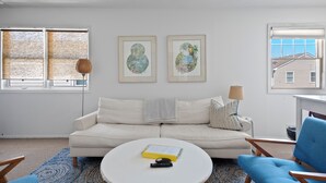 Un salon avec un canapé blanc, une table basse ronde et deux œuvres d’art encadrées accrochées au mur.