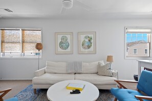 A living room with a white sofa, a round coffee table, and two framed artworks on the wall.