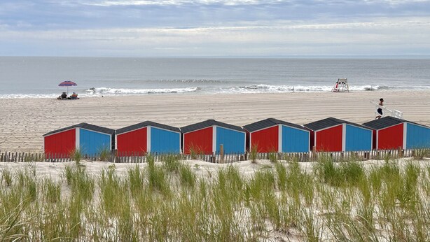 Une plage bordée d’une rangée de cabanes de plage colorées, avec un poste de surveillance des sauveteurs et l’océan en arrière-plan.