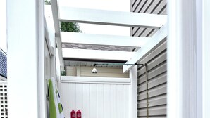 Une terrasse en bois avec une porte blanche, une serviette à rayures vertes et blanches, et une petite étagère avec des bouteilles rouges.