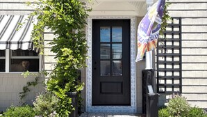 Une maison avec une porte d’entrée noire, un petit porche avec des marches et un drapeau sur la droite.