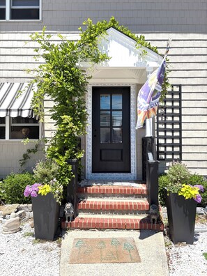 A house with a black front door, a small porch with steps, and a flag on the right.