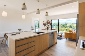 Uma cozinha moderna com uma ilha grande, luminárias pendentes e vista para o campo.