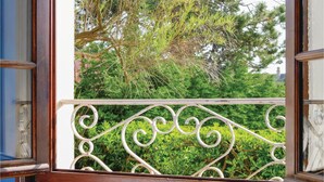 Un balcon doté de balustrades en métal blanc ouvragées, offrant une vue sur un paysage verdoyant composé de feuillages et d’arbres.
