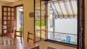 Une pièce avec une table à manger en bois, des chaises, une fenêtre avec des rideaux à rayures et une vue sur un jardin.