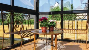 Une véranda avec une table ronde et deux chaises, des plantes en pot et une vue sur l’extérieur.