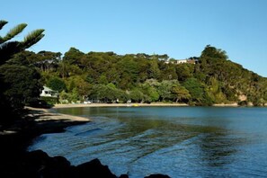 Eine Küstenlandschaft mit Strand, Bäumen und einem Gebäude auf einem Hügel.