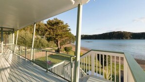 Une terrasse en bois dotée d’une balustrade, qui offre une vue sur un lac et des collines boisées.
