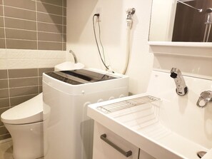 Un bagno compatto con il water, una lavatrice e un lavandino dotato di rubinetto.