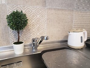 Una cucina con lavello, una pianta in vaso, un bollitore ed uno schienale decorato.
