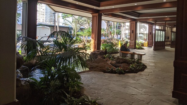 Un vestíbulo amplio con suelo de piedra, ventanas grandes y plantas de interior.
