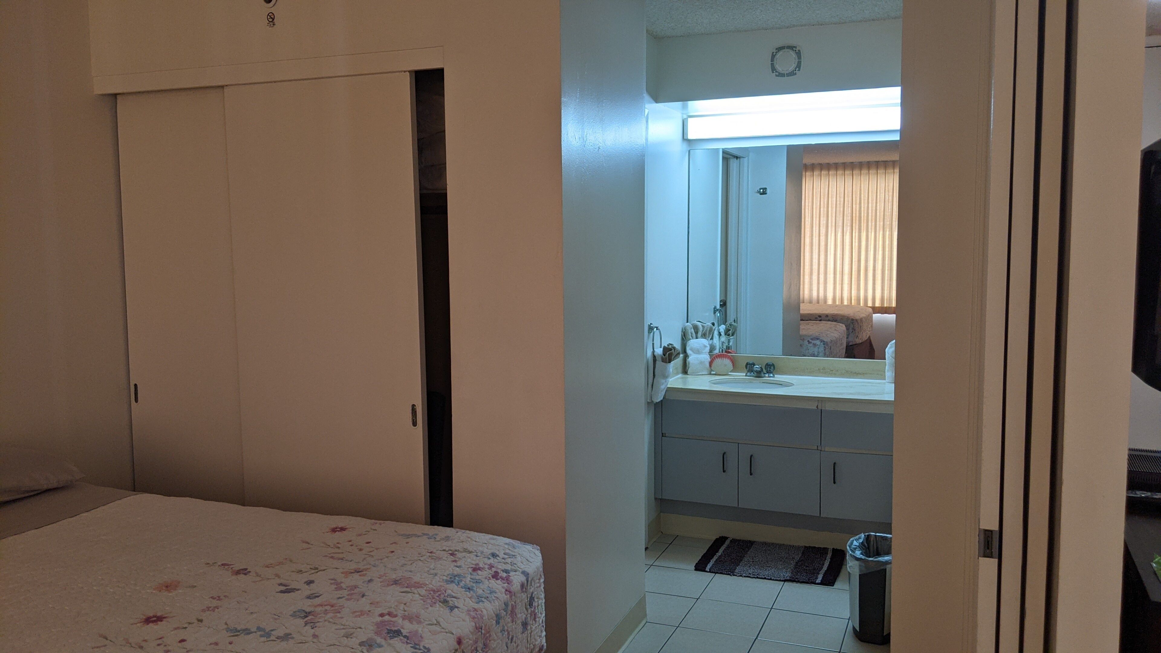 A bedroom with a bed, a bathroom with a sink, mirror, and toilet.