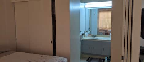 A bedroom with a bed, a bathroom with a sink, mirror, and toilet.