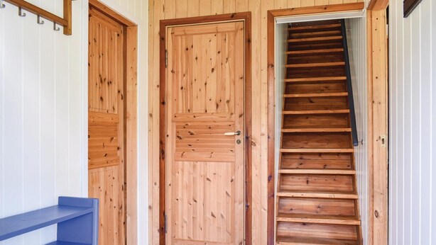 Eine Holztreppe führt zu einer zweiten Etage, begleitet von zwei Holztüren mit Metallgriffen.