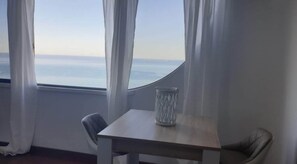 Enjoy a serene sea view from the comfort of this stylish room, featuring a large window, a small table, and two chairs.
