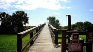 A wooden boardwalk leading to a beach, with signs warning about dunes and snakes.
