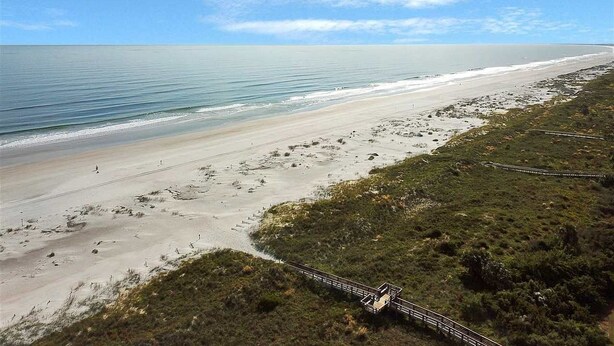 A beach with a wooden boardwalk leading to the shore, sandy beach, and ocean.