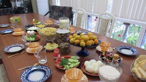 Una mesa de comedor dispuesta con diferentes platos, frutas, verduras y bebidas.
