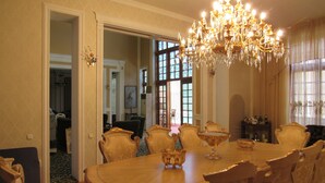 Un comedor formal con una gran mesa de madera, sillas ornamentadas, una araña y vistas a través de un ventanal.