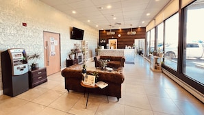 A hotel lobby with a reception desk, seating area, and an ATM machine. - Camrose LeChateau Hotel (Camrose)