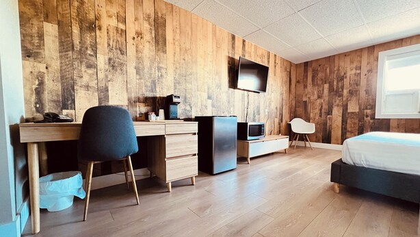 A modern bedroom with a wooden wall, a bed, a desk with a chair, a TV, and a microwave. - Camrose LeChateau Hotel (Camrose)
