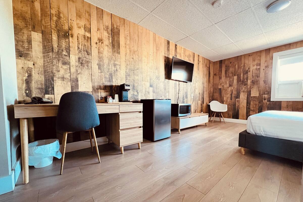 Une chambre moderne avec un mur en bois, un lit, un bureau avec une chaise, une télévision et un four à micro-ondes.