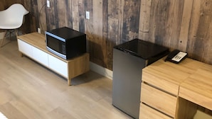 A modern hotel room with a wooden wall, a flat-screen TV, a microwave, a refrigerator, a desk with drawers, and a white chair. - Camrose LeChateau Hotel (Camrose)