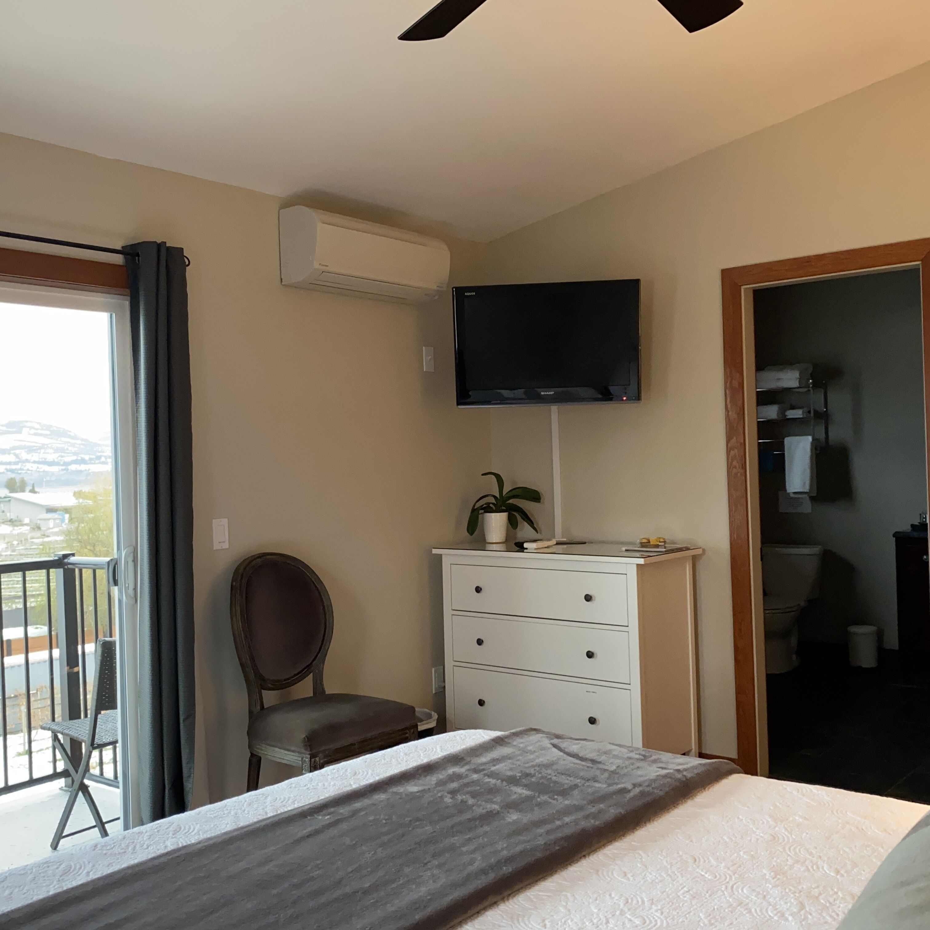 A bedroom with a bed, a dresser, a chair, a TV mounted on the wall, and an air conditioning unit.