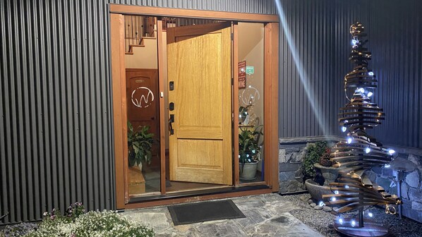 Entrada de hotel con una puerta de madera, una puerta de vidrio y una escultura de luz decorativa en el exterior.