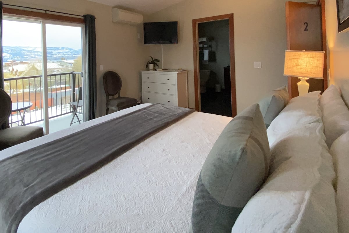 A hotel room with a large bed, a chair, a dresser, a TV, and a balcony with a view.