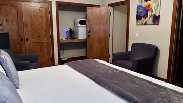 Un dormitorio con una cama, una silla, un armario, un microondas y un estante con un hervidor.