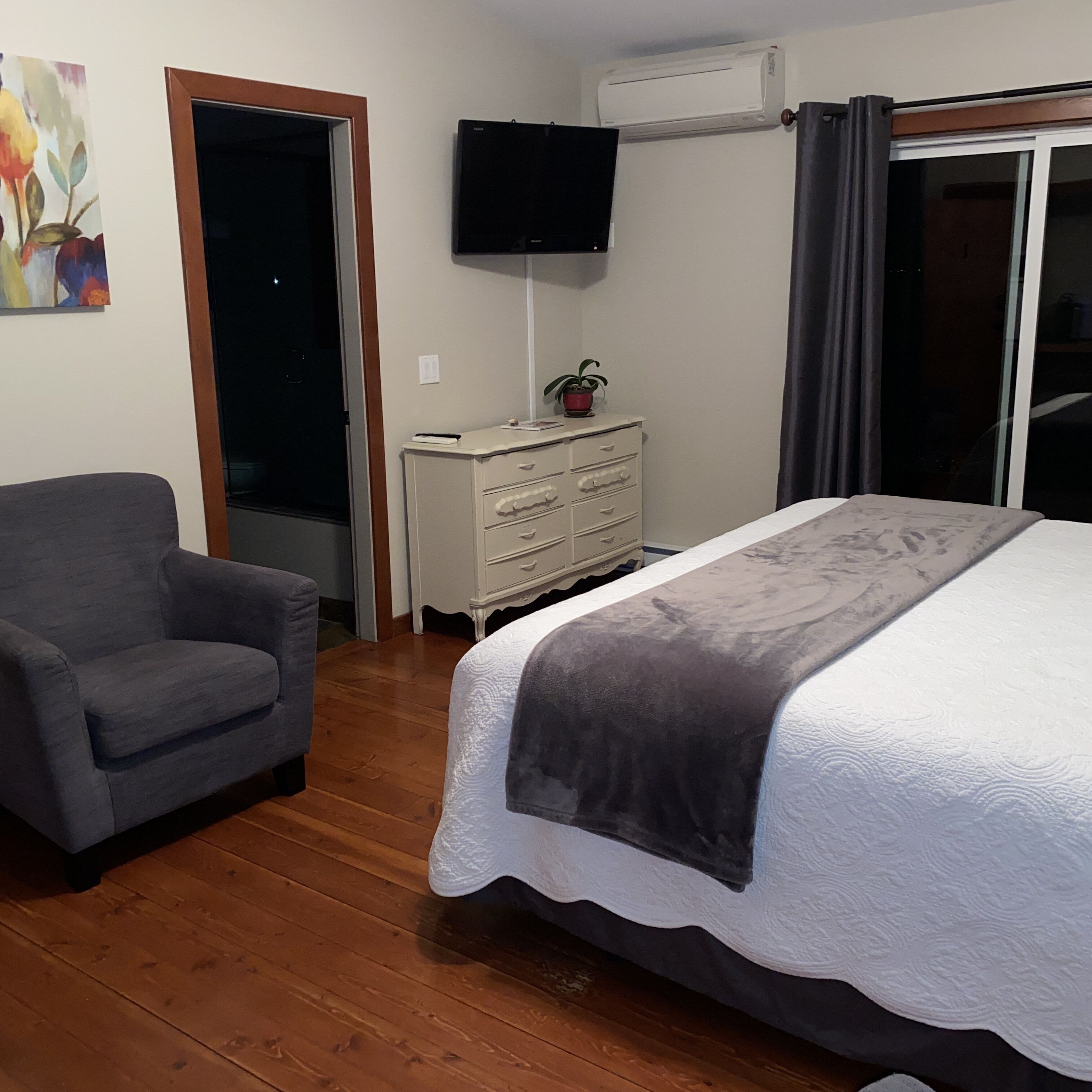 A bedroom with a bed, a chair, a dresser, an air conditioner, and a TV.