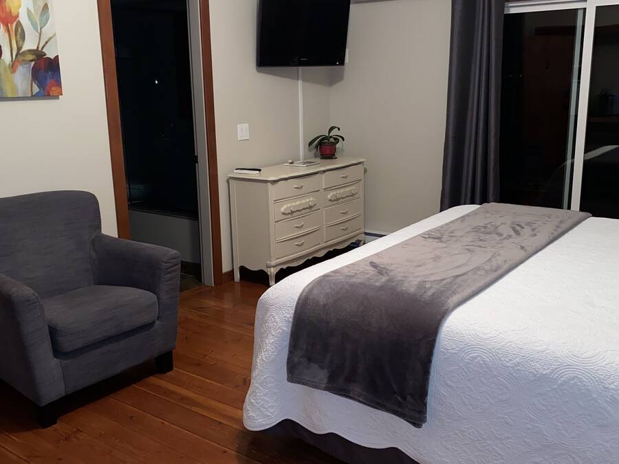 A bedroom with a bed, a chair, a dresser, an air conditioner, and a TV.