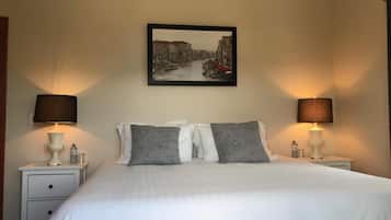 A neatly made bed with white linens and two pillows, flanked by bedside tables with lamps and a framed picture above.